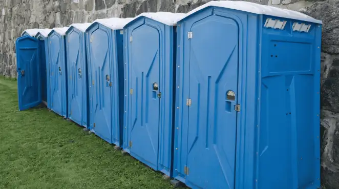 Row of blue portable toilets lined up on grass against a stone wall for event sanitation in Henderson, NV