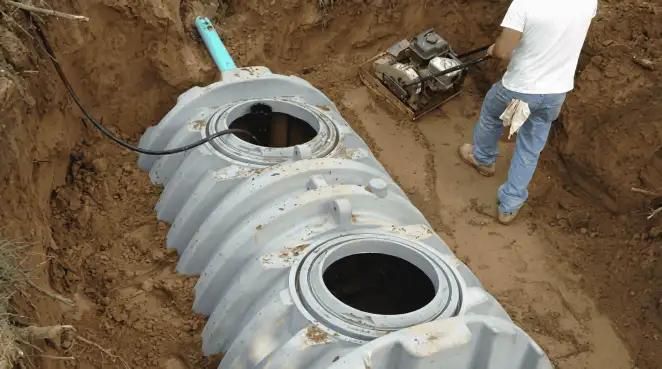 Septic tank installation showing a technician compacting soil around a new poly septic tank in an excavation pit in Henderson, NV